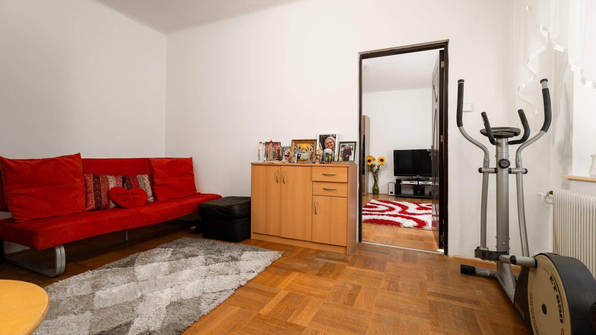 Vielseitiger Raum mit rotem Sofa, Parkettboden und Heimtrainer.