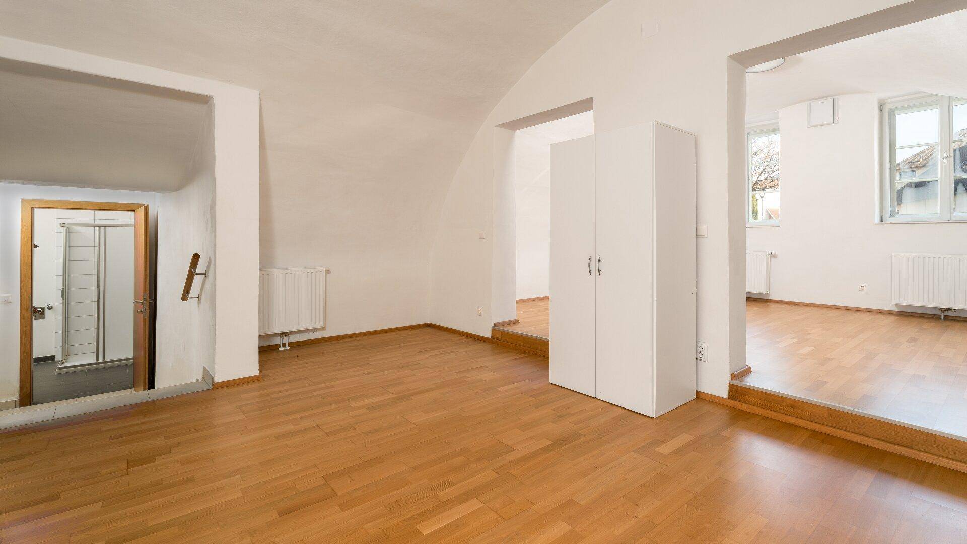 Heller Wohnraum mit Parkettboden und Zugang zu einem weiteren Zimmer sowie einem Badezimmer.