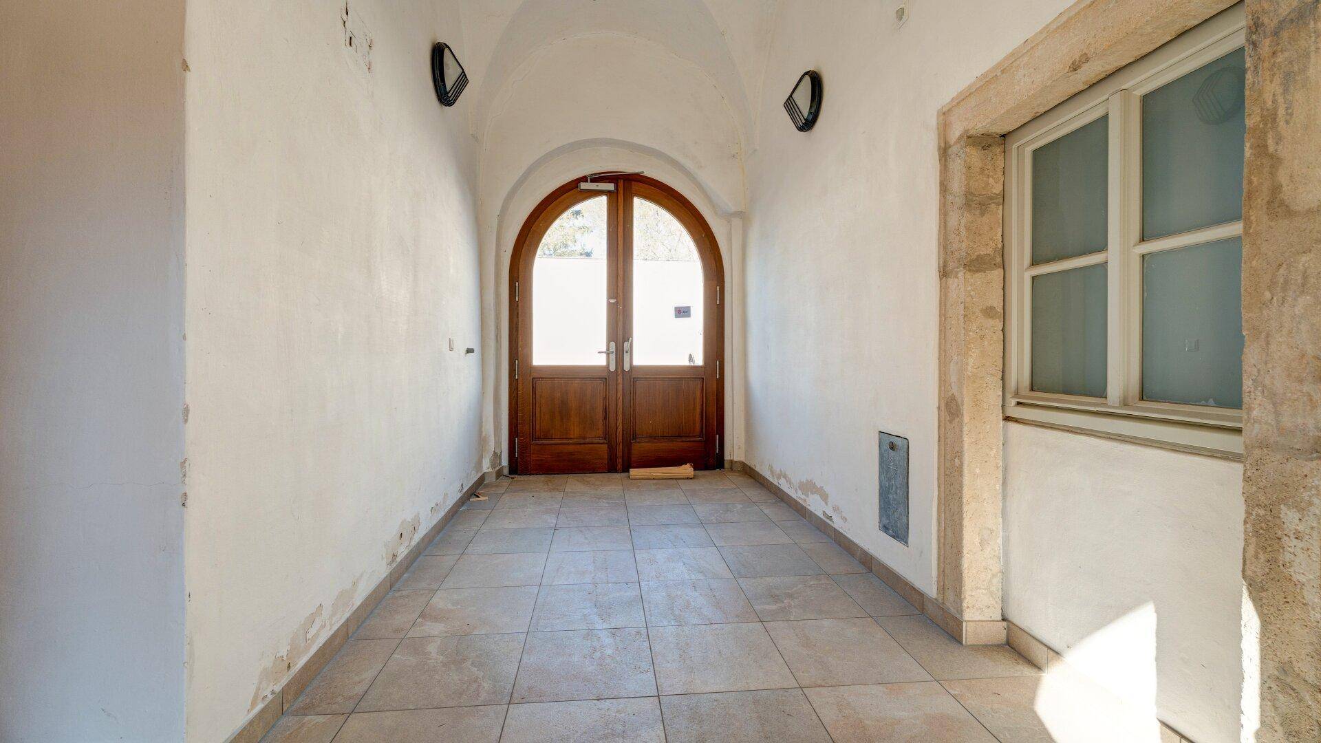 Historischer Eingangsbereich mit gewölbter Decke, Holztüren und gefliestem Boden in einem alten Gebäude.