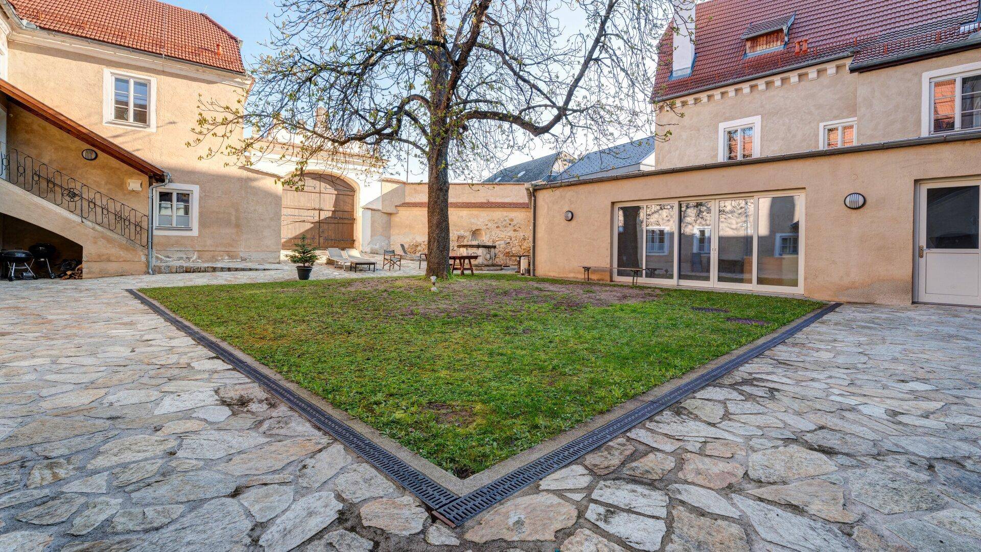 Weitläufiger Innenhof mit gepflasterten Wegen, zentraler Rasenfläche und Zugang zu den Gebäuden.