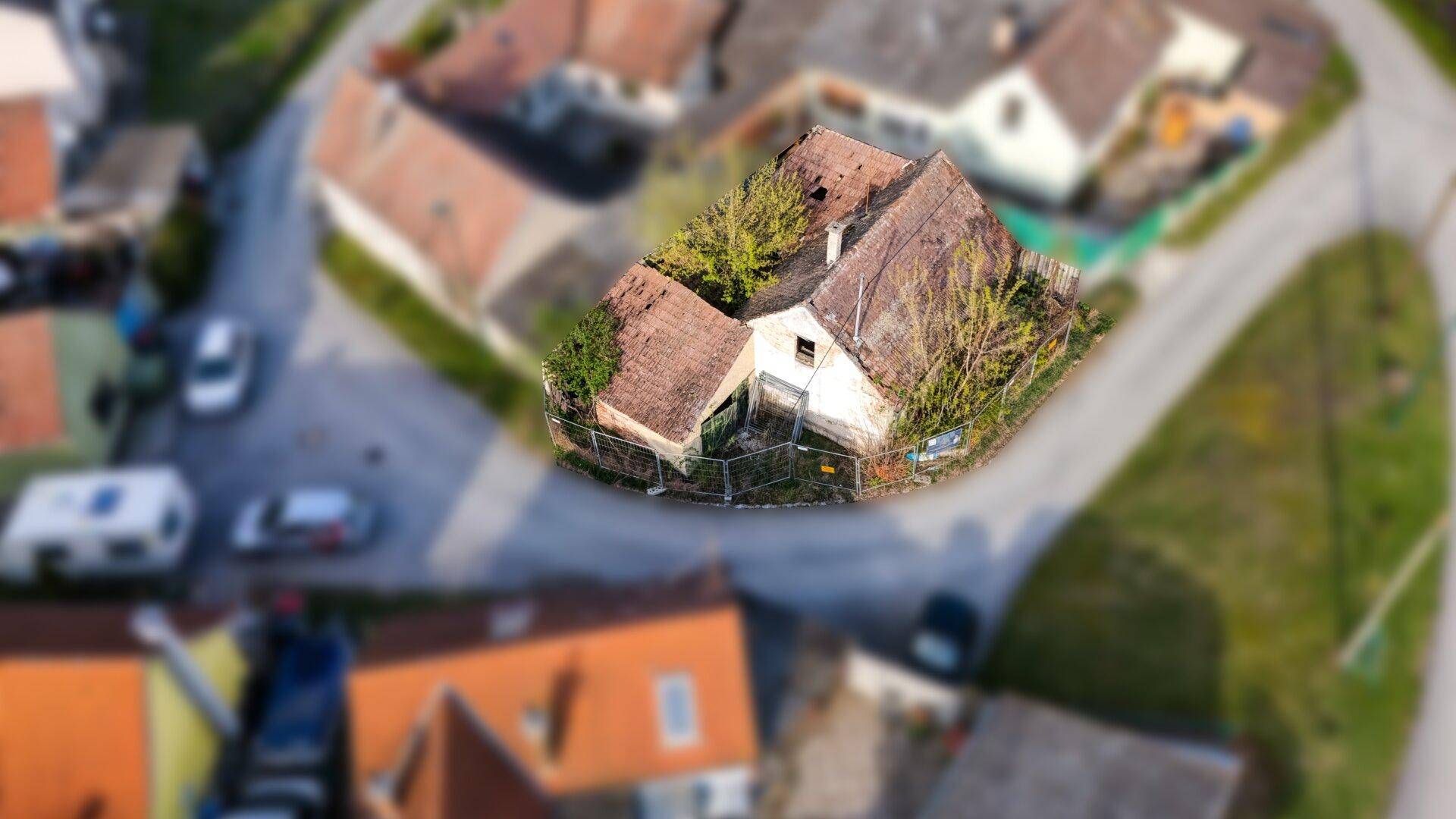 Schrägansicht aus der Luft auf ein sanierungsbedürftiges Haus mit verwildertem Grundstück.