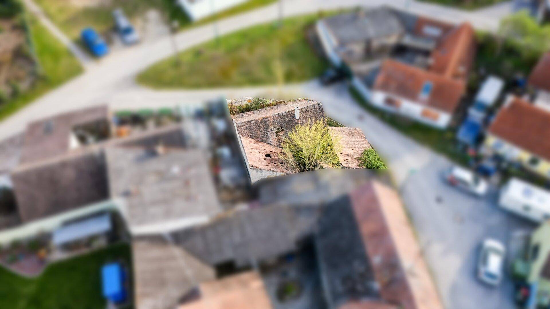 Draufsicht auf ein älteres Gebäude mit verwildertem Grundstück und angrenzenden Straßen in einer Siedlung.