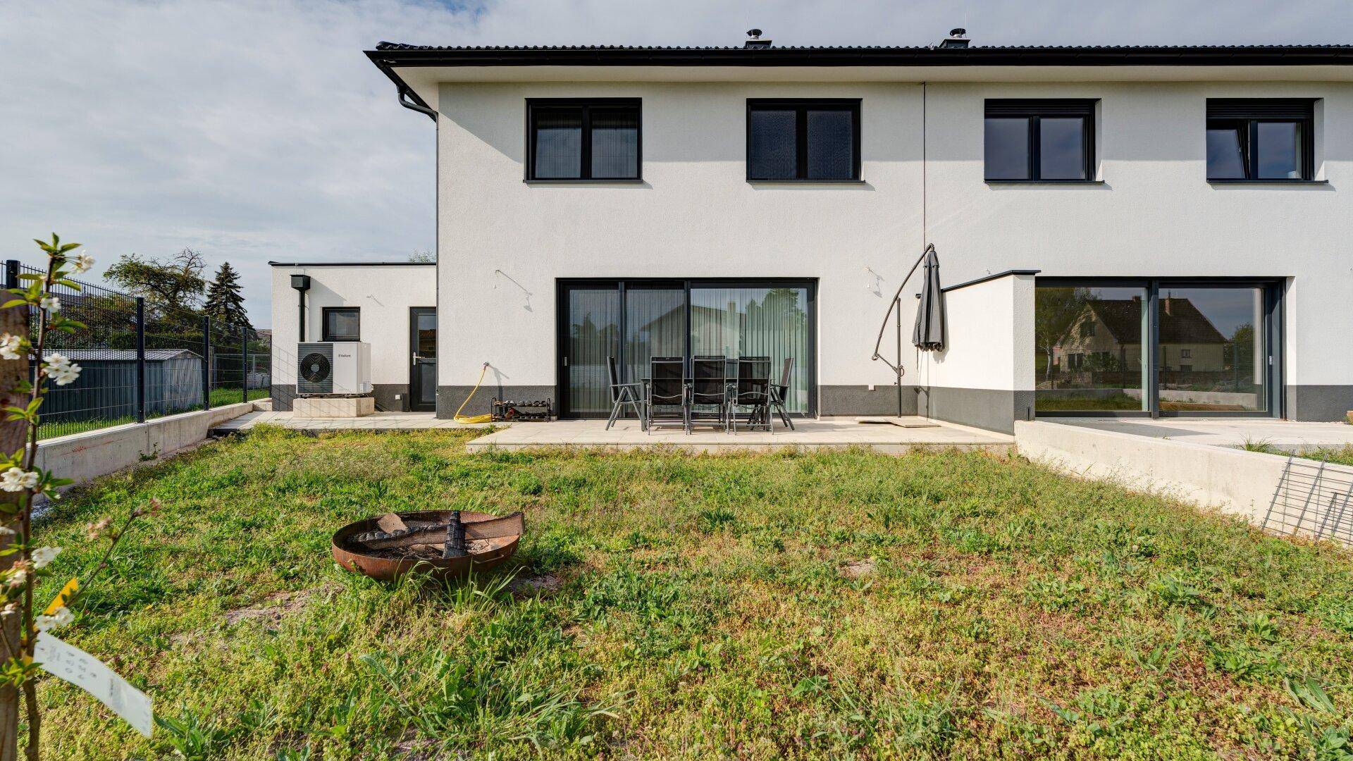 Hinterer Gartenbereich mit Terrasse, Schiebetüren und Blick auf die grüne Umgebung.