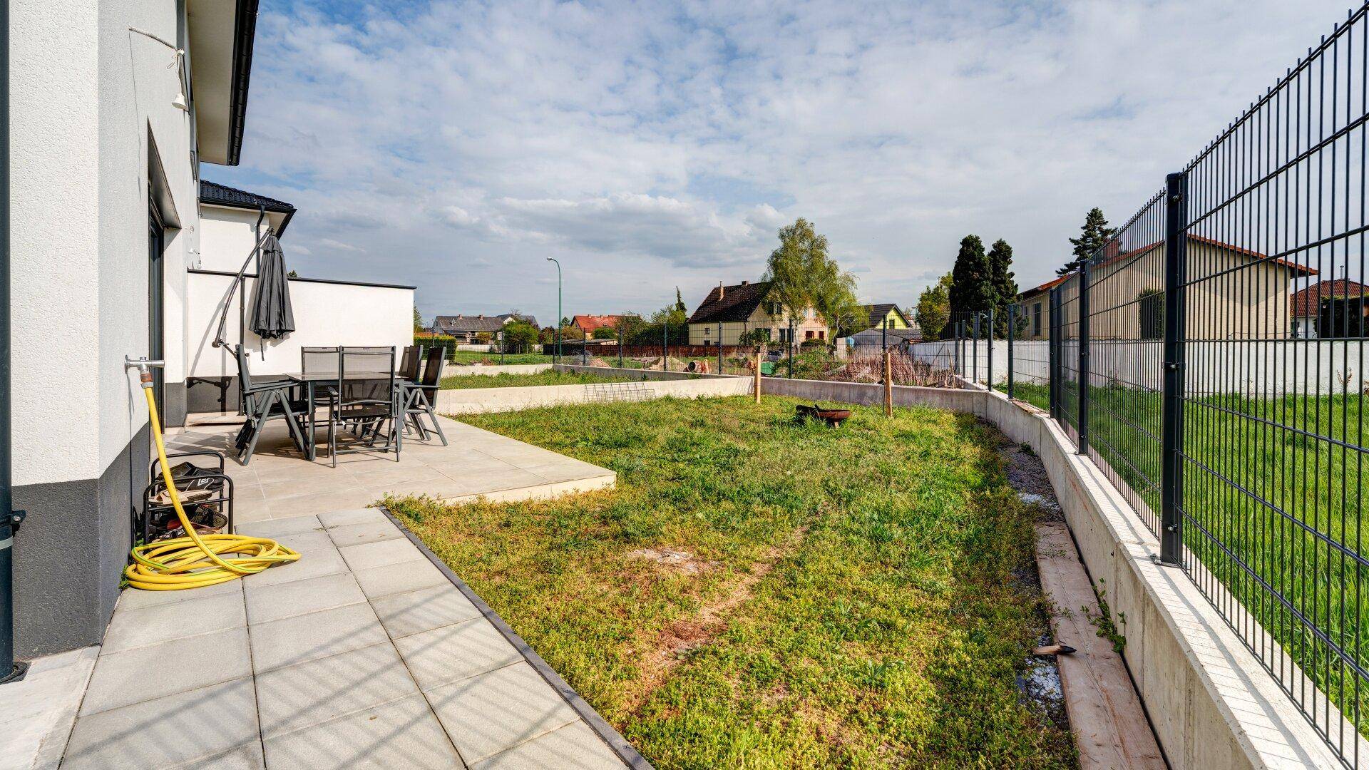 Ungepflegter Gartenbereich mit Terrasse, Zaun und Blick auf die Nachbarschaft.