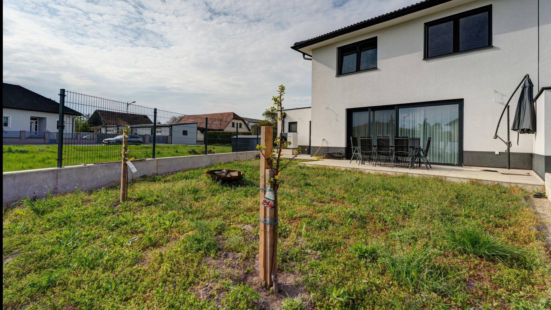 Hinterer Gartenbereich mit Terrasse, jungen Bäumen und Blick auf die Umgebung.