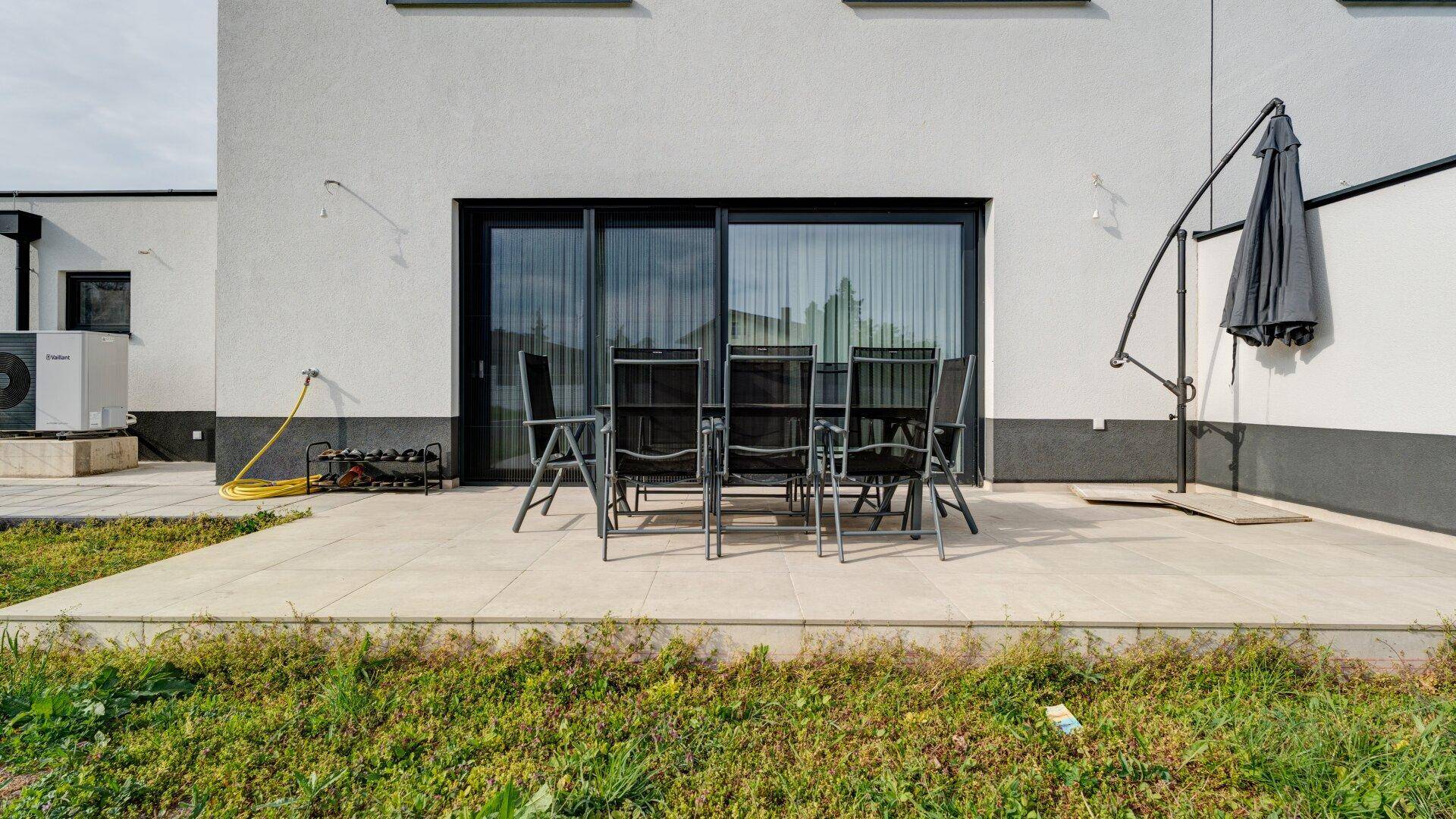 Gepflasterte Terrasse mit Gartenmöbeln und großzügigen Schiebetüren zum Haus.