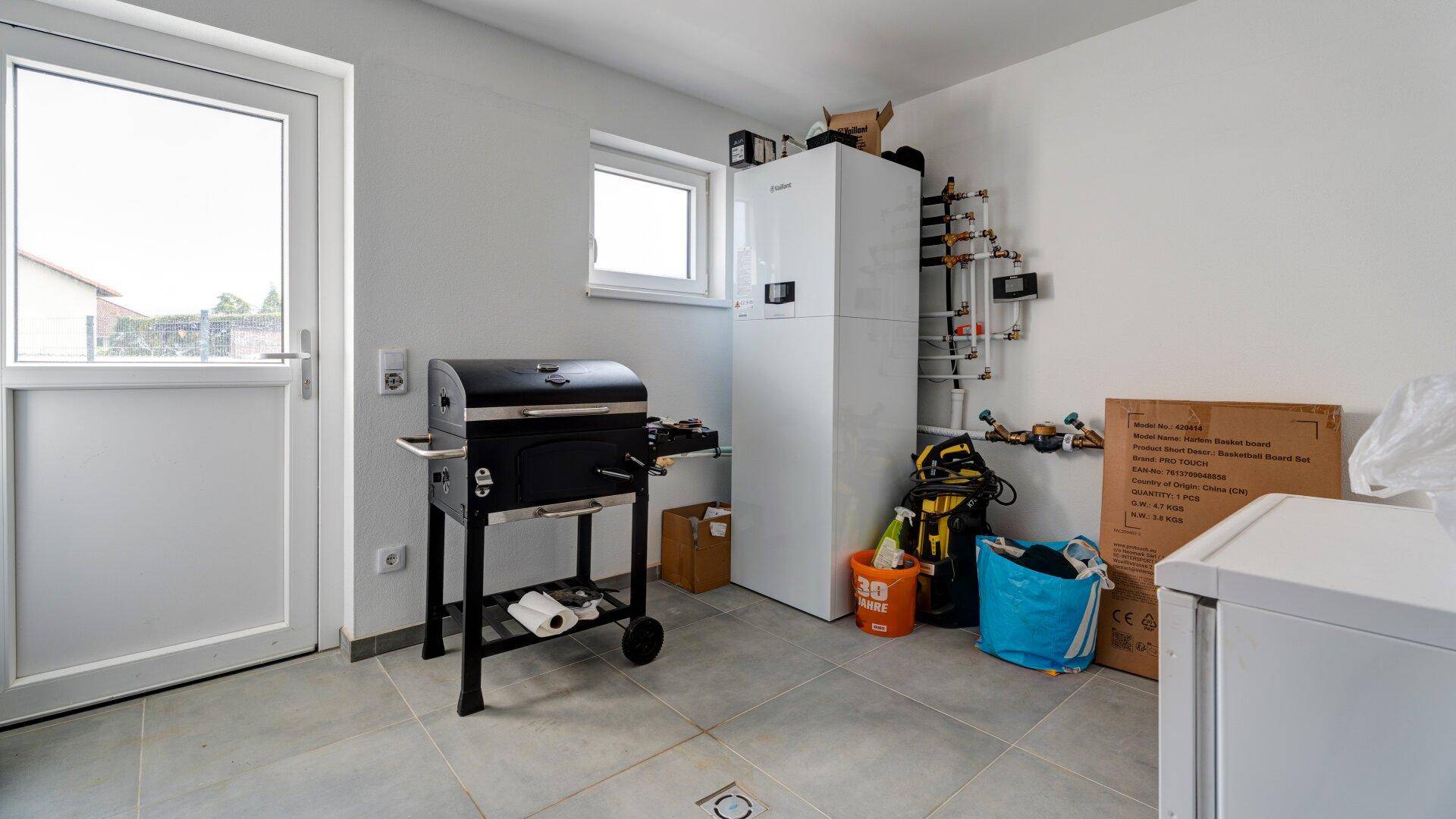 Hauswirtschaftsraum mit Heizungsanlage, Grill und Zugang nach draußen.