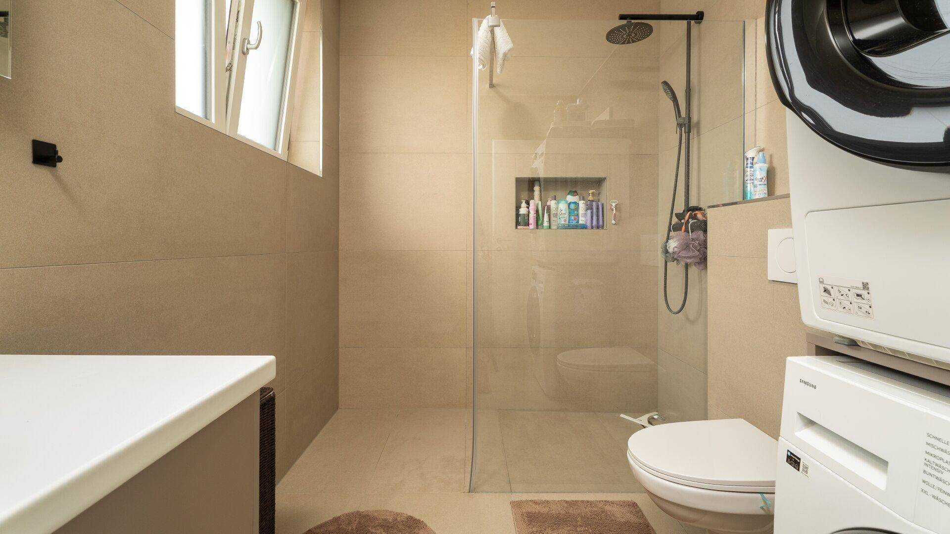 Geräumiges Badezimmer mit begehbarer Dusche, WC und Waschmaschine.
