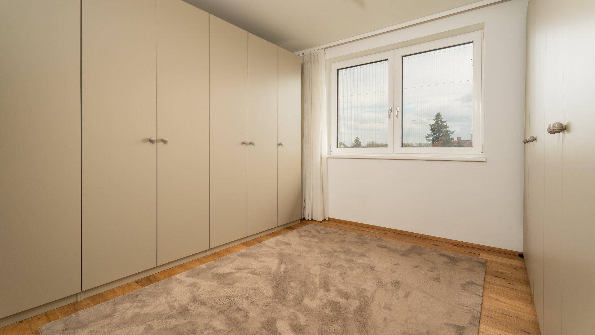 Heller Ankleidebereich mit Einbauschränken und Fenster.
