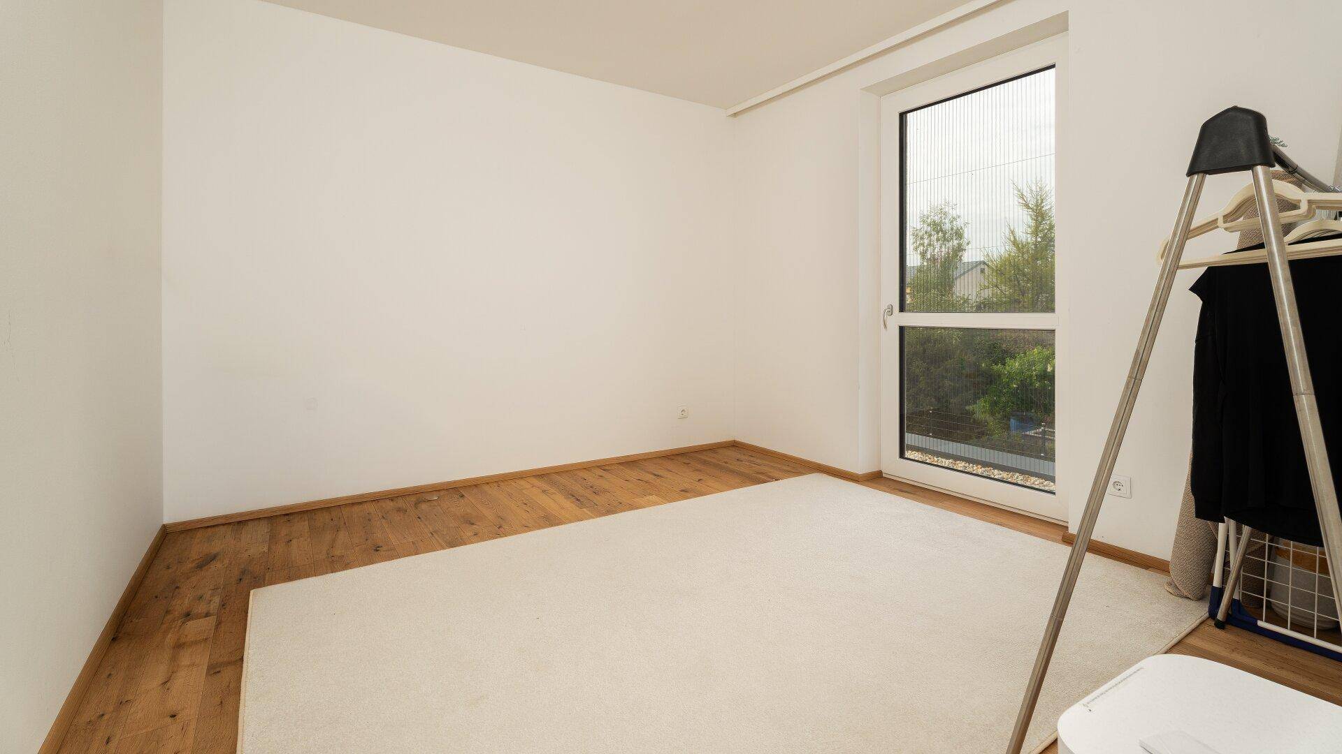 Leeres Zimmer mit Holzboden und Zugang zum Außenbereich.