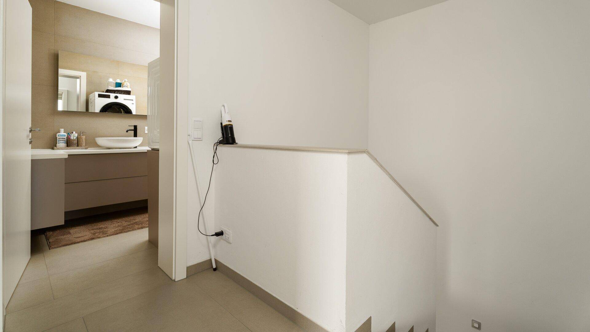 Heller Flur mit Blick auf ein modernes Badezimmer und Treppenaufgang.