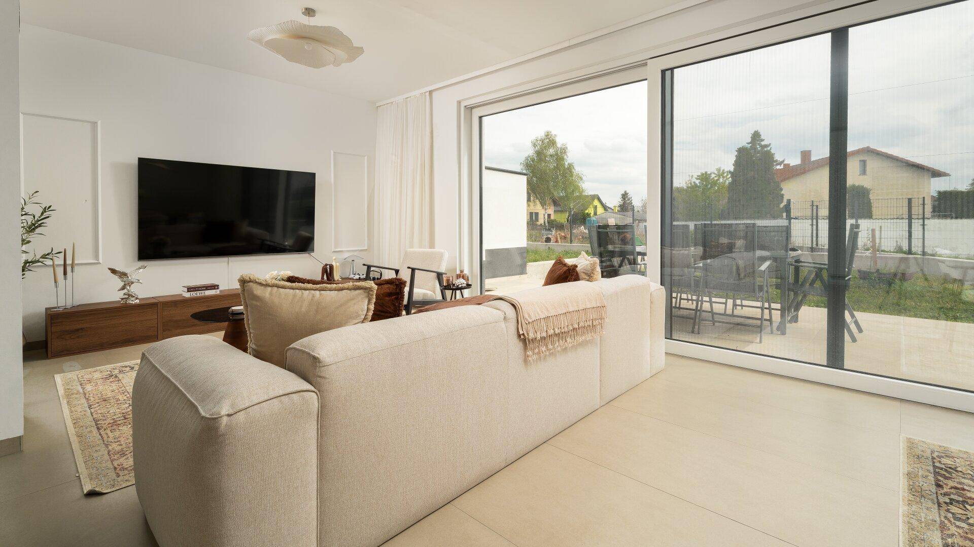 Heller Wohnbereich mit beigem Sofa, großen Fenstern und direktem Zugang zum Garten.