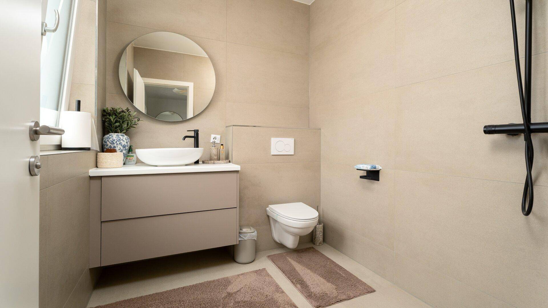 Kleines Badezimmer mit beigen Fliesen, wandhängendem WC und modernem Waschtisch.