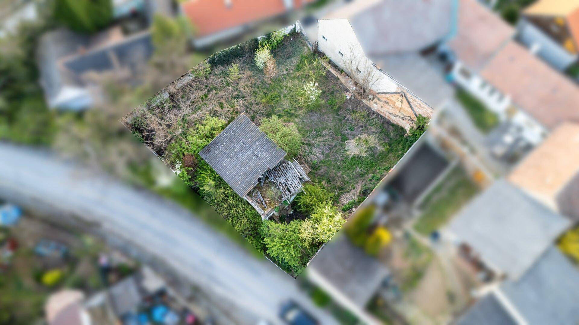 Luftaufnahme eines Grundstücks mit einem kleinen, baufälligen Gebäude und viel Grünfläche in einer Wohngegend.