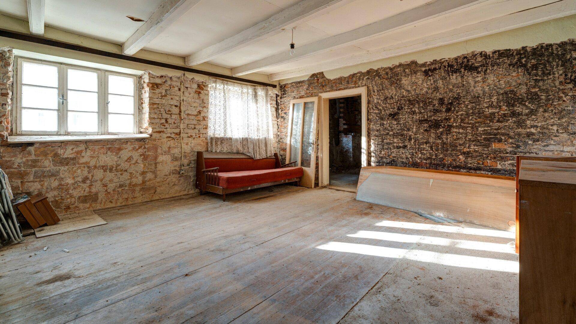 Helles Wohnzimmer mit alten Holzdielen, freiliegenden Deckenbalken und viel natürlichem Licht durch große Fenster.
