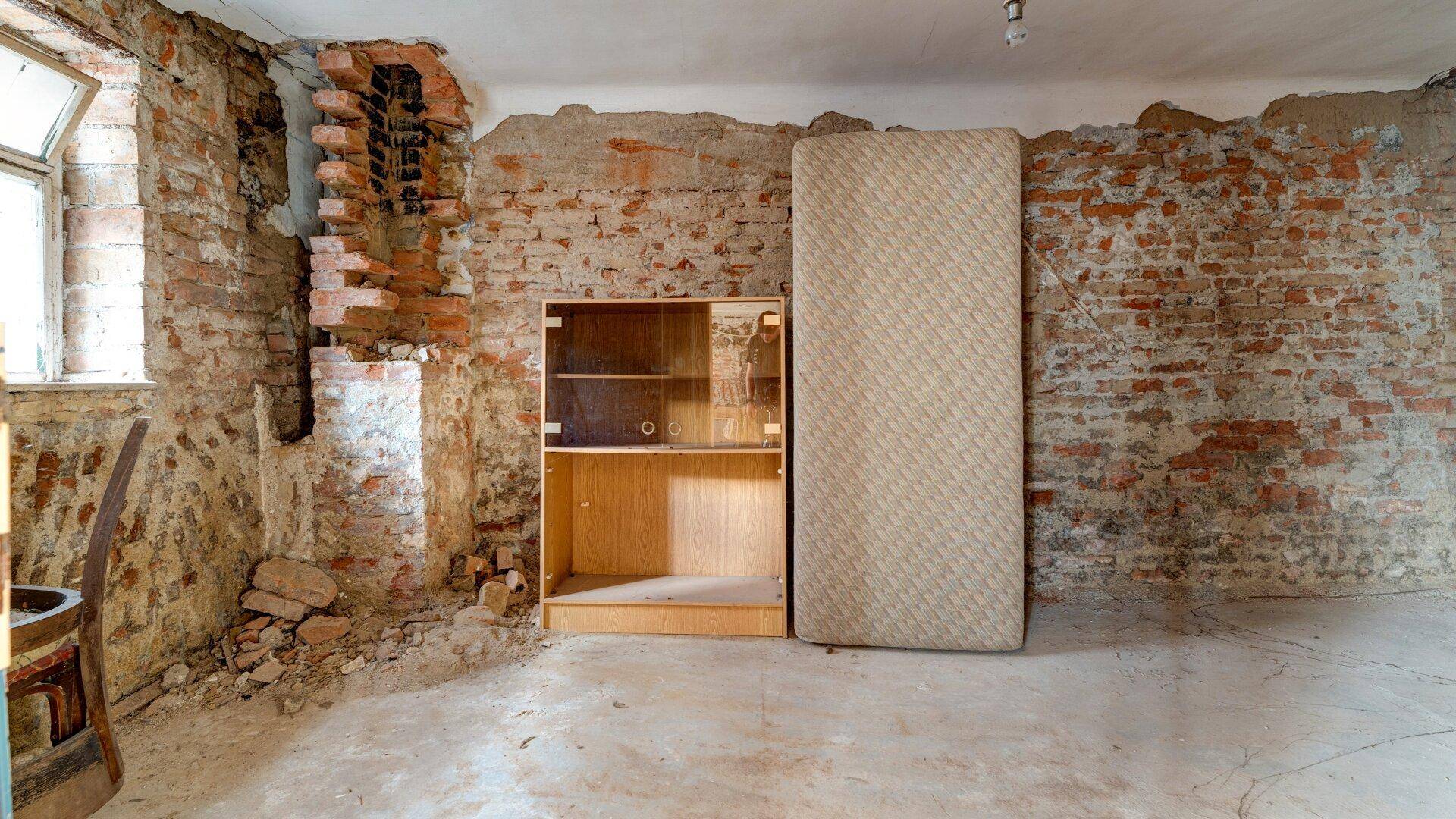Schlafzimmer im Rohbauzustand mit freiliegenden Ziegelwänden, Fenster und einem Schrank.