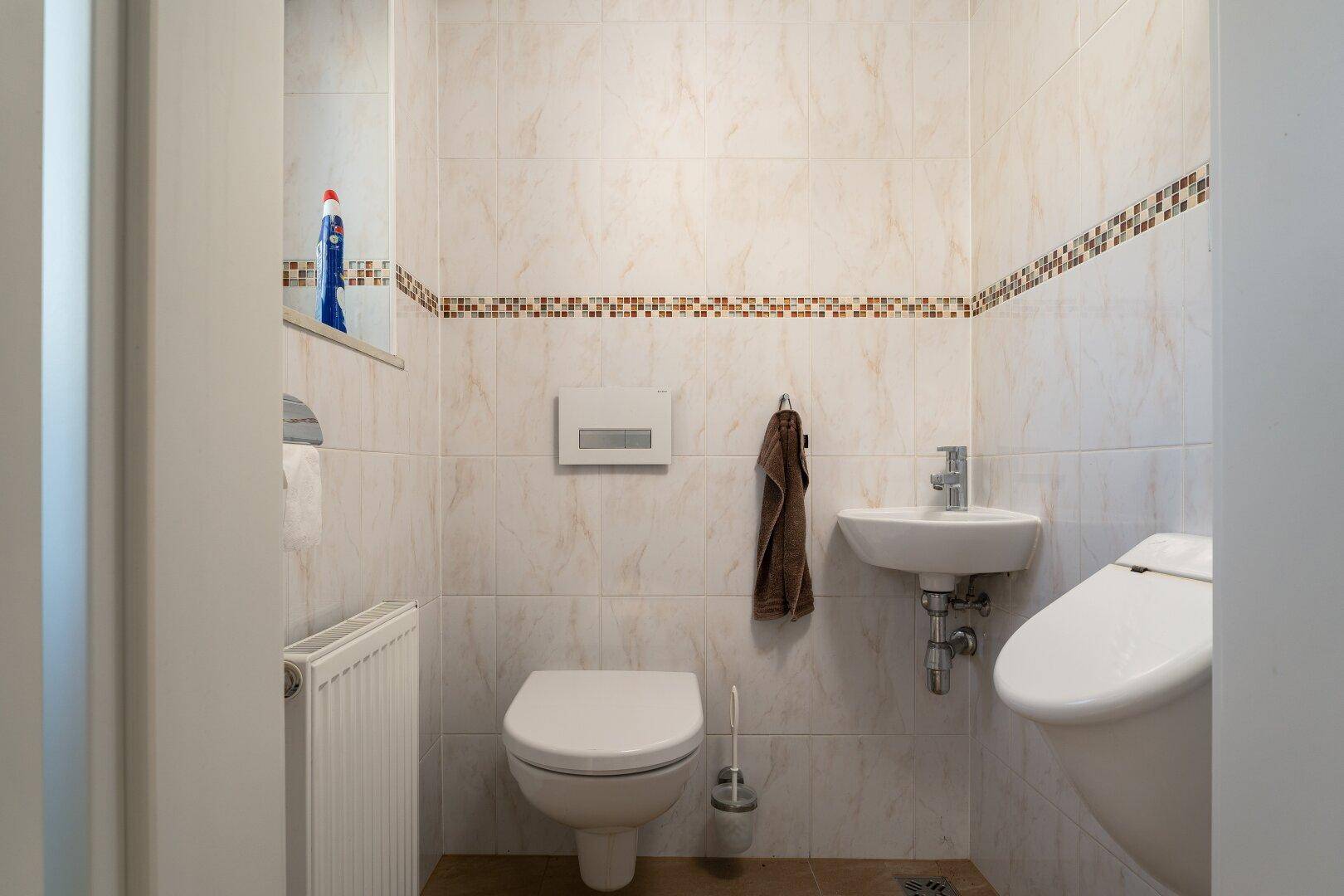 Kleines WC mit beigen Fliesen, Mosaikbordüre und wandhängendem WC.