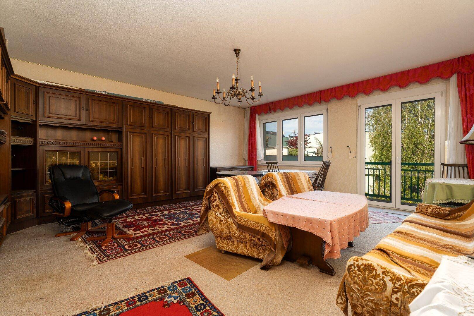 Traditionelles Wohnzimmer mit Teppichboden, Holzmöbeln und Zugang zum französischen Balkon.