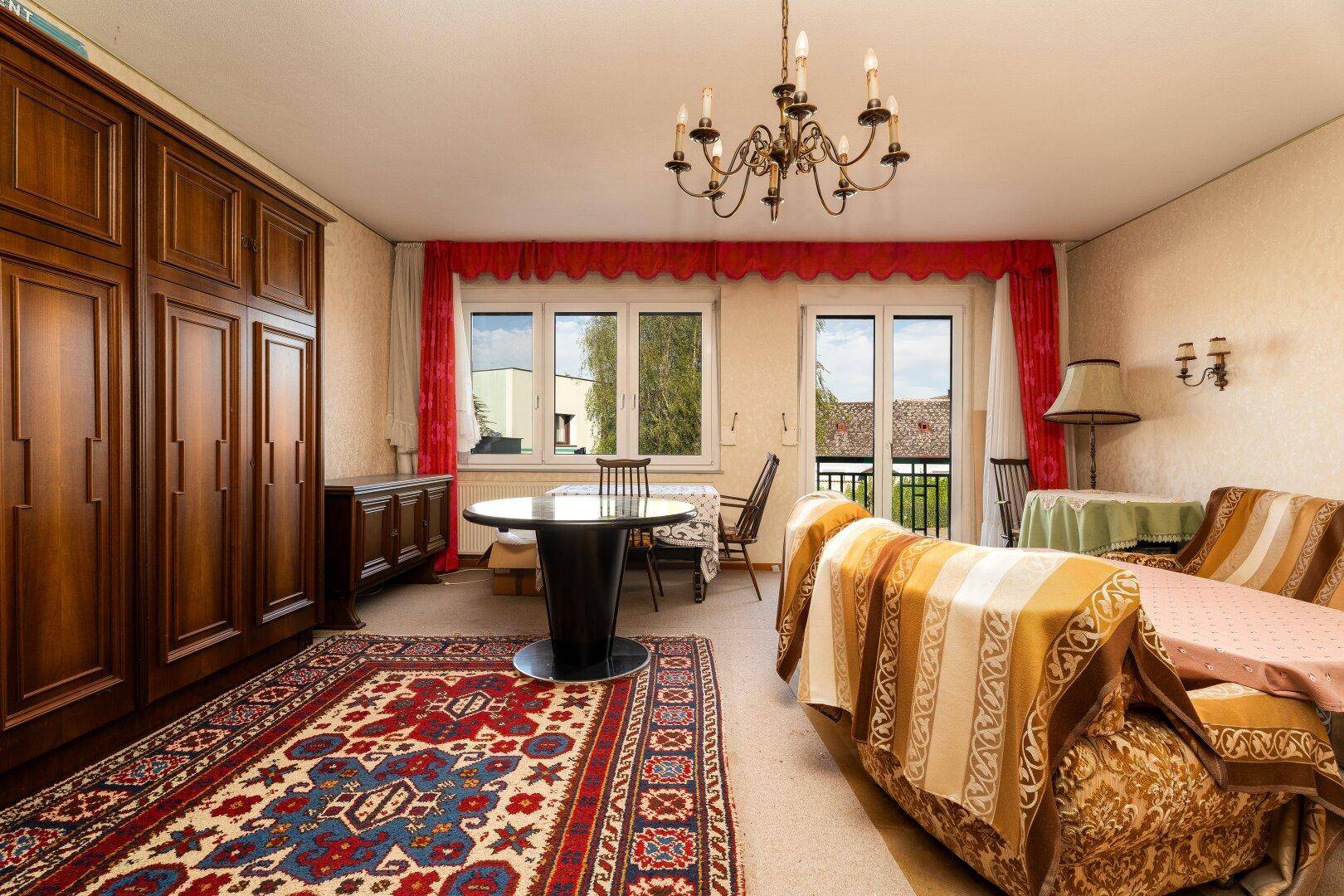 Gemütliches Wohnzimmer mit klassischem Kronleuchter, Teppichboden und Holzmöbeln.