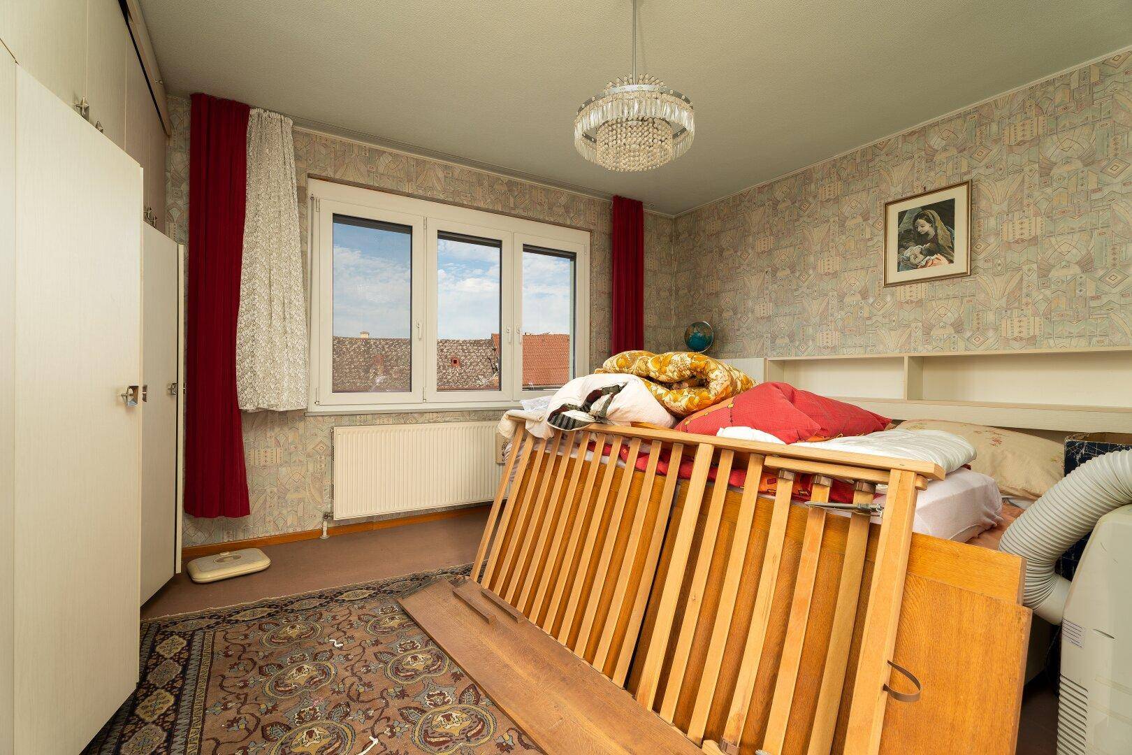 Schlafzimmer mit Teppichboden, großem Fenster und Babybett.