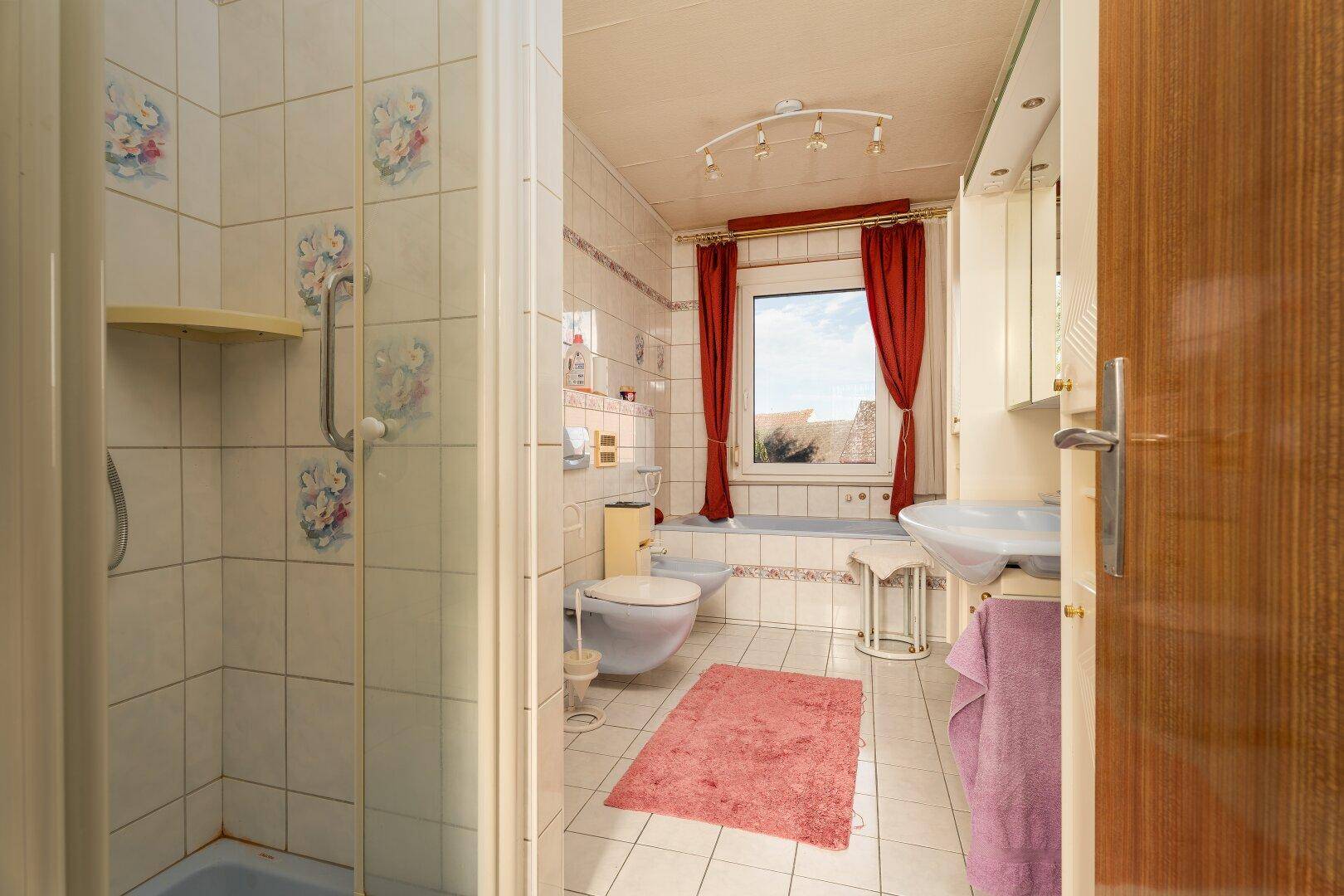 Badezimmer mit weißen Fliesen, Dusche, Badewanne und Fenster.