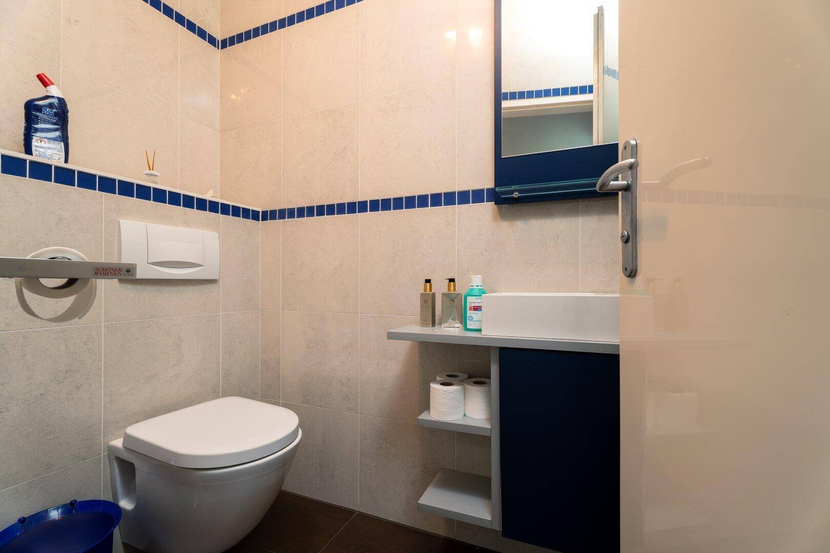 Gäste-WC mit hellen Fliesen, blauen Akzenten und wandhängendem WC.