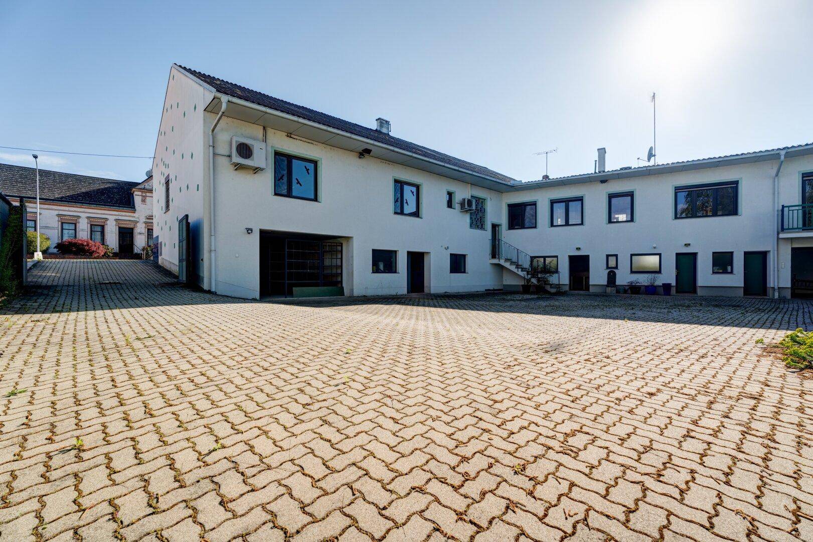 Weitläufiger gepflasterter Hof vor einem weißen Gebäude unter strahlendem Sonnenschein.