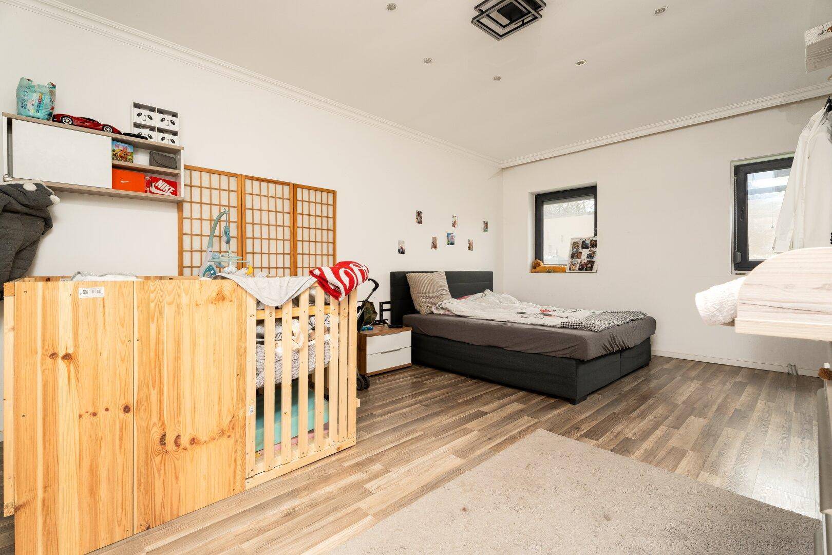 Ein Schlafzimmer mit einem Doppelbett, einem Babybett und Laminatboden in Holzoptik.