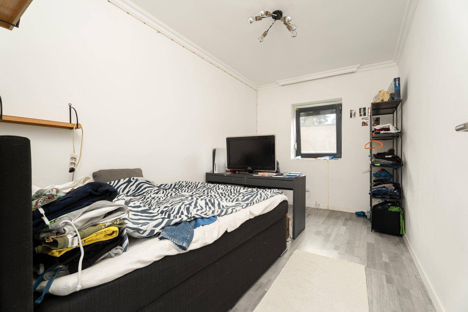 Ein kleines Schlafzimmer mit einem Einzelbett, einem Fernseher und hellgrauem Laminatboden.
