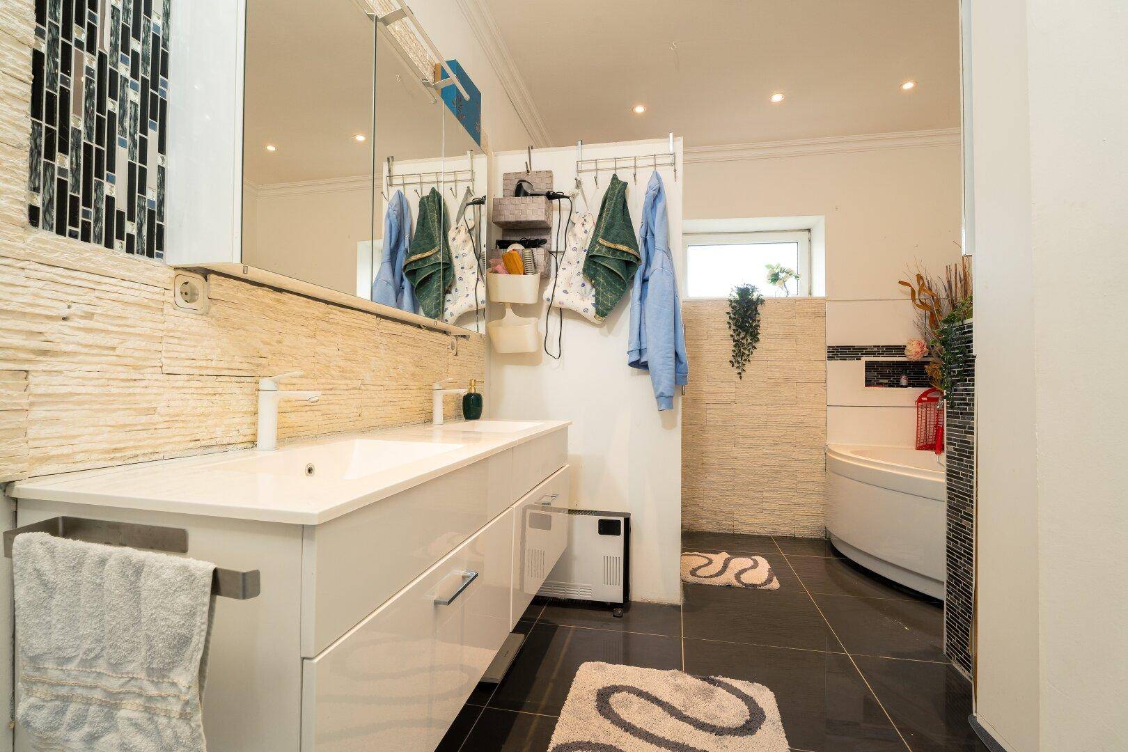 Ein modernes Badezimmer mit einem großen Waschtisch, einer Eckbadewanne und dunklen Fliesenböden.