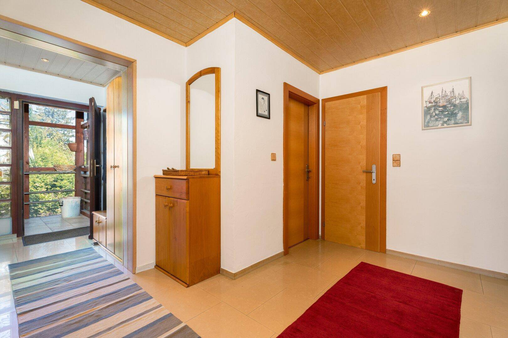 Heller Eingangsbereich mit Fliesenboden, Holzdecke und Garderobenmöbeln.