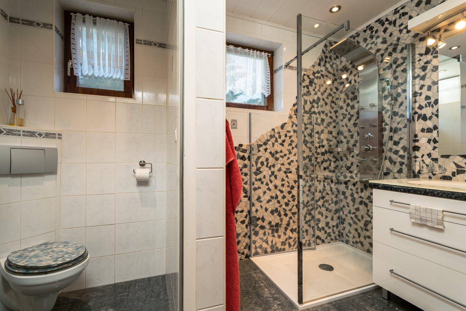 Modernes Badezimmer mit begehbarer Dusche, Mosaikfliesen und zwei Fenstern.