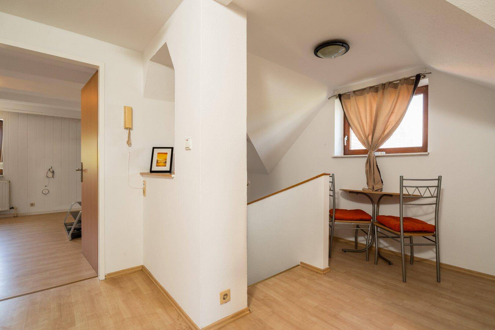 Heller Dachgeschossflur mit Holzboden, kleiner Sitzecke und Zugang zu weiteren Räumen.