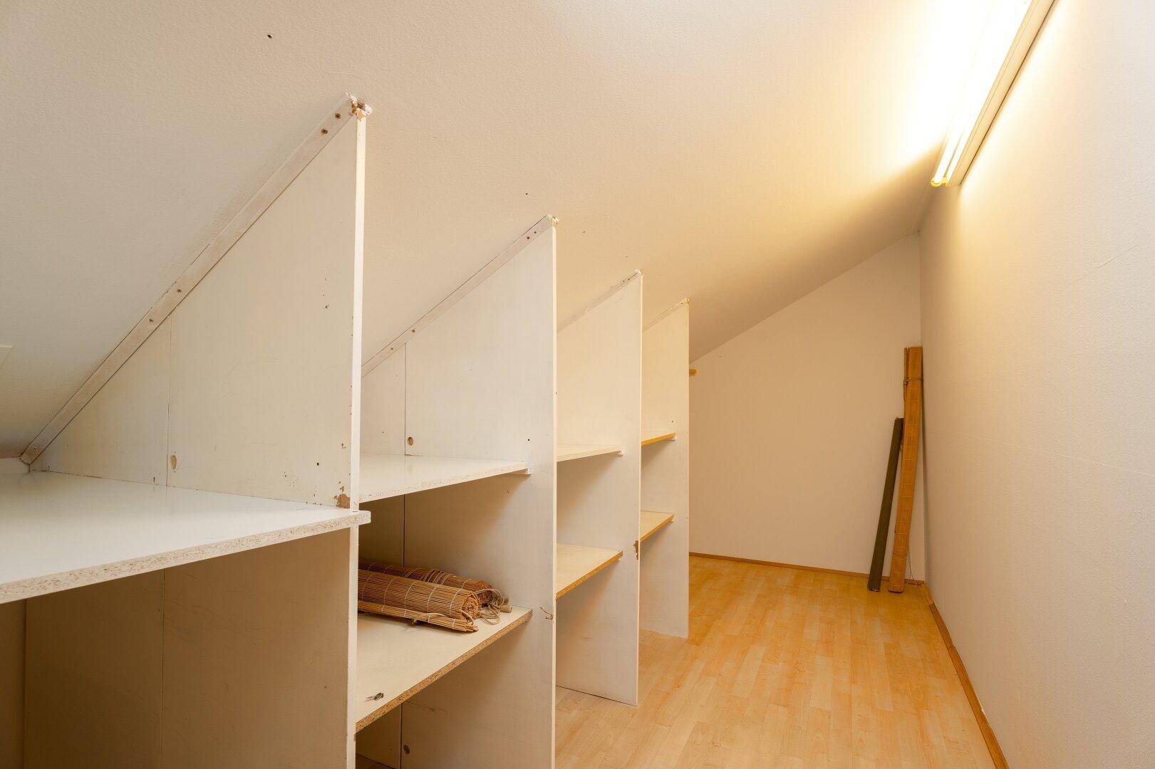 Praktischer Abstellraum im Dachgeschoss mit eingebauten Regalen und Holzboden.