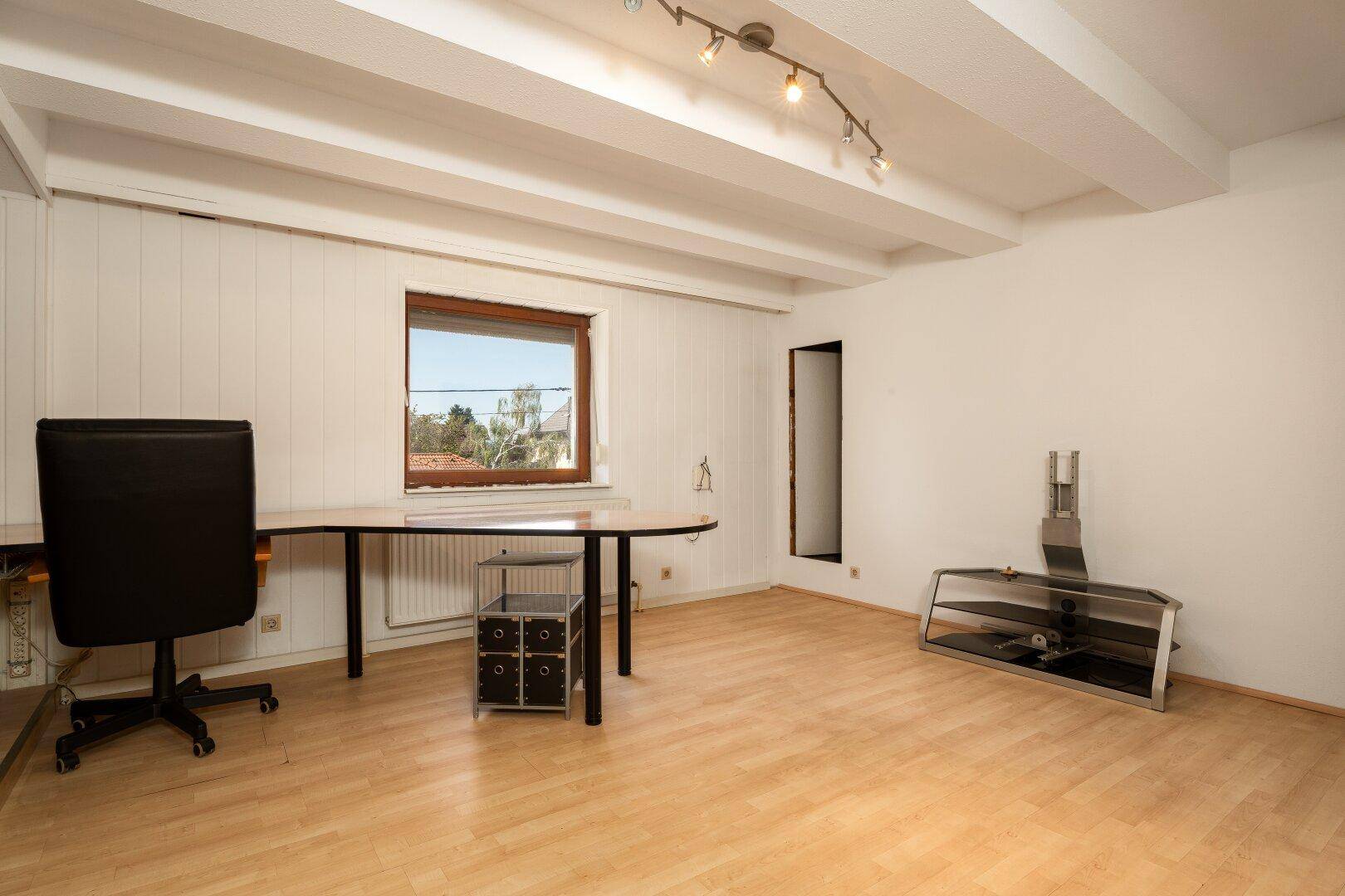 Geräumiges Dachgeschosszimmer mit Holzboden, Deckenbalken und Blick ins Freie.