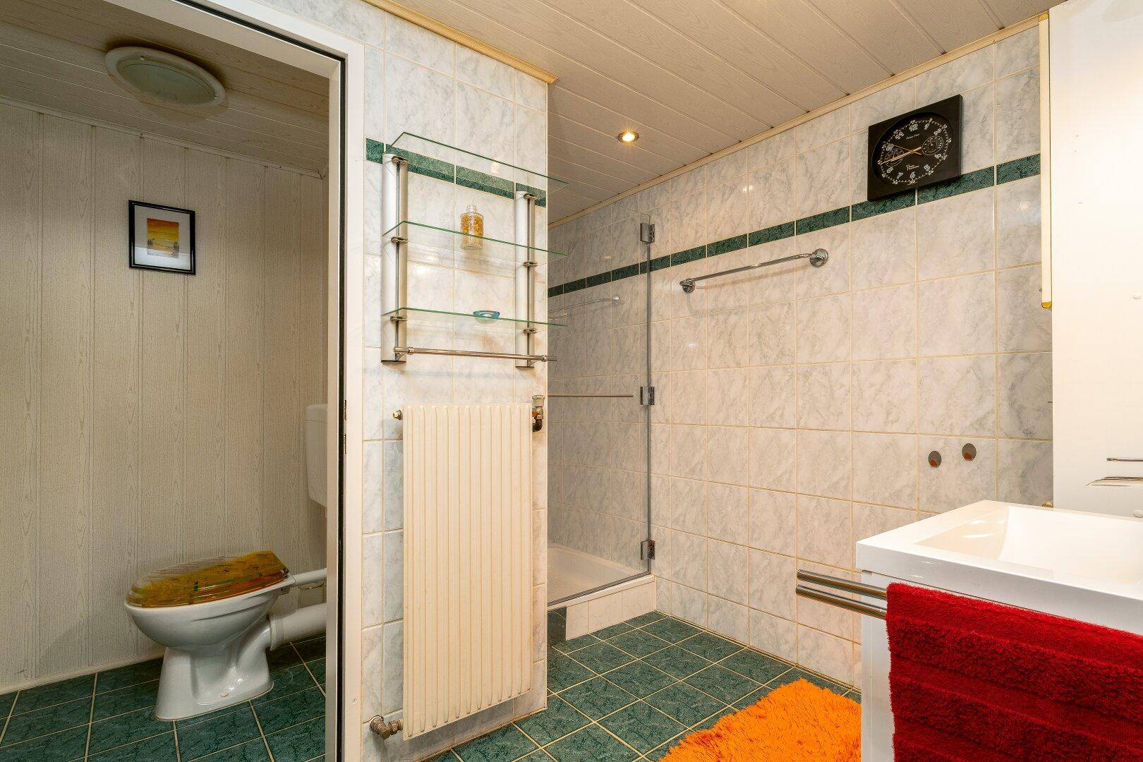 Funktionales Badezimmer im Untergeschoss mit Dusche, Fliesenboden und Holzdecke.