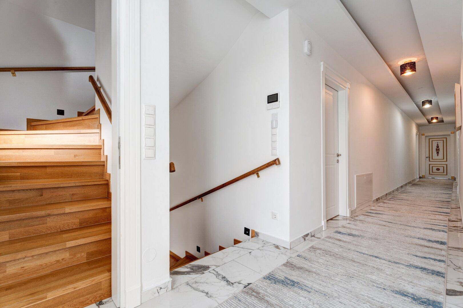 Heller Flur mit eleganter Holztreppe und modernem Marmorboden im Eingangsbereich.