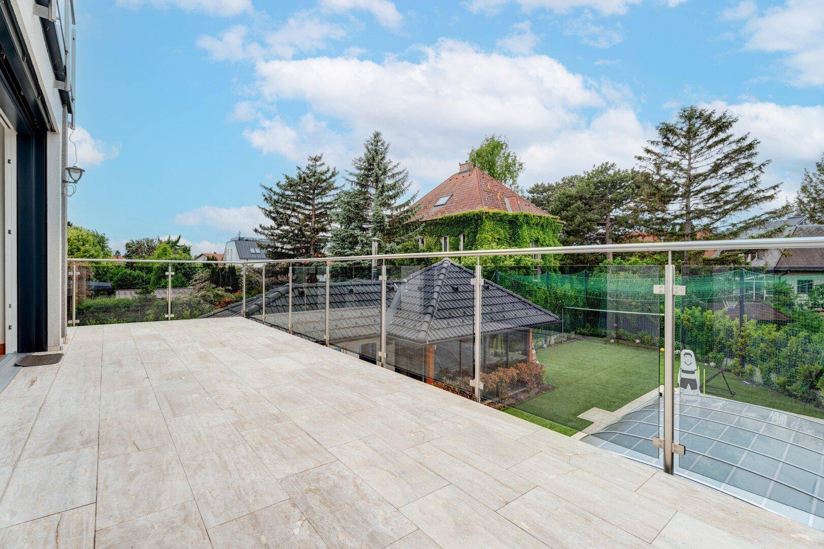 Große Terrasse mit modernem Glasgeländer und Blick auf den Garten und die Nachbarschaft.