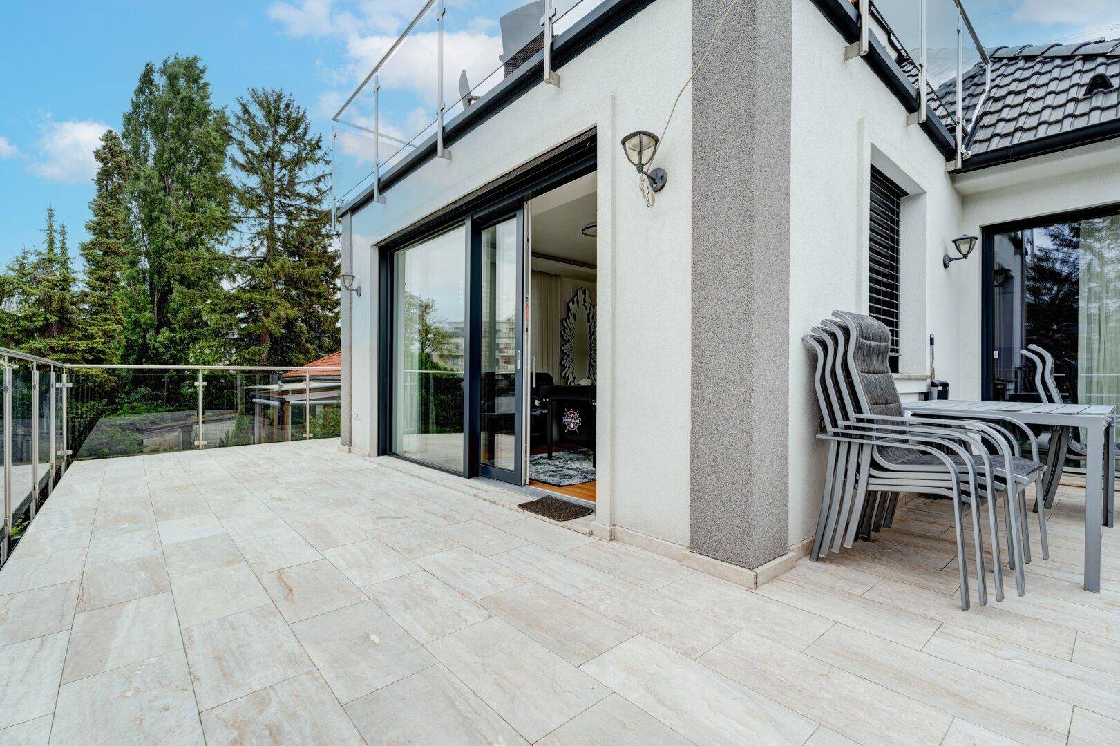 Terrasse mit Schiebetüren zum Innenbereich und gestapelten Gartenstühlen für gesellige Stunden.