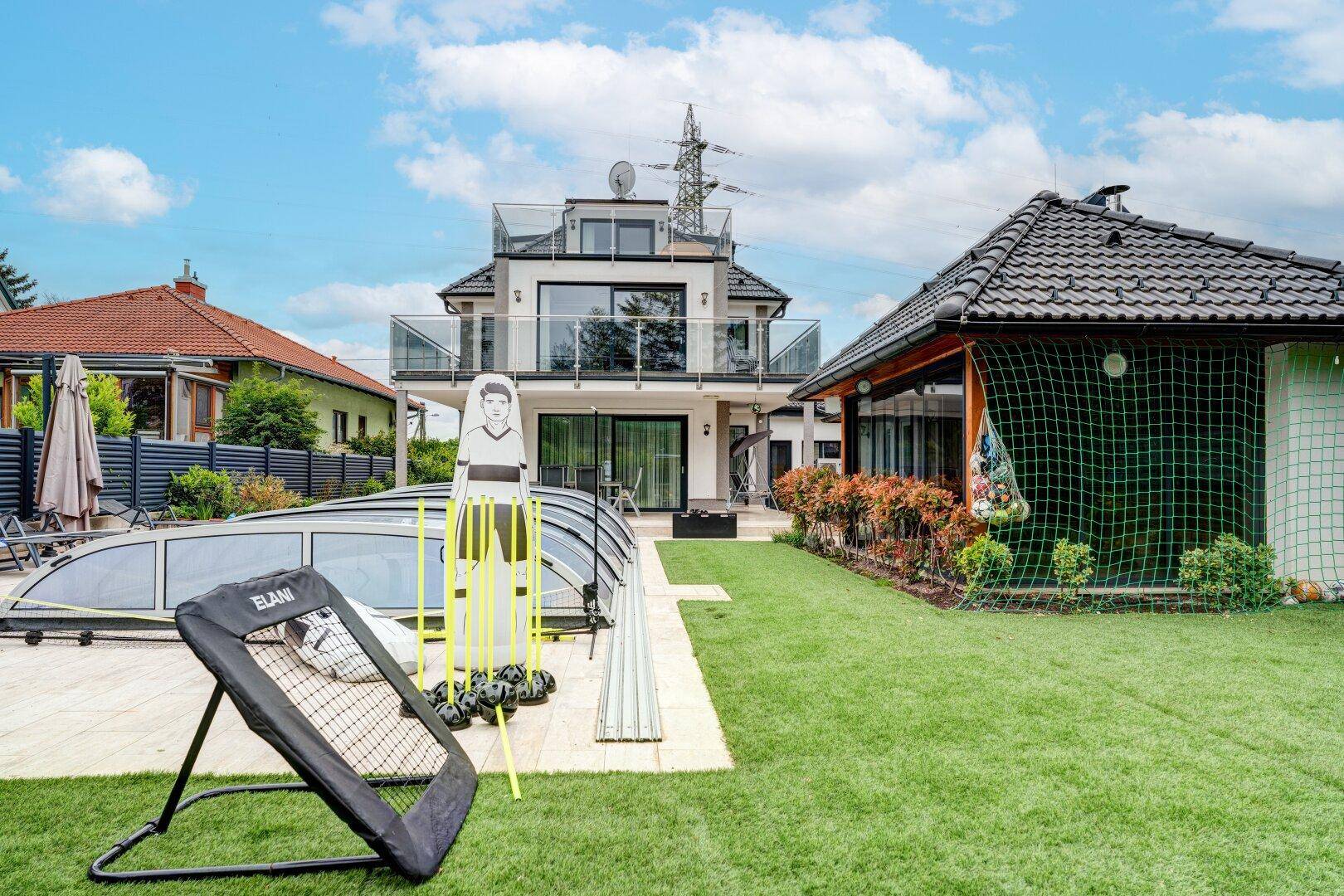 Gartenbereich mit Pool, Rasenfläche und Sportgeräten für Freizeitaktivitäten im Freien.