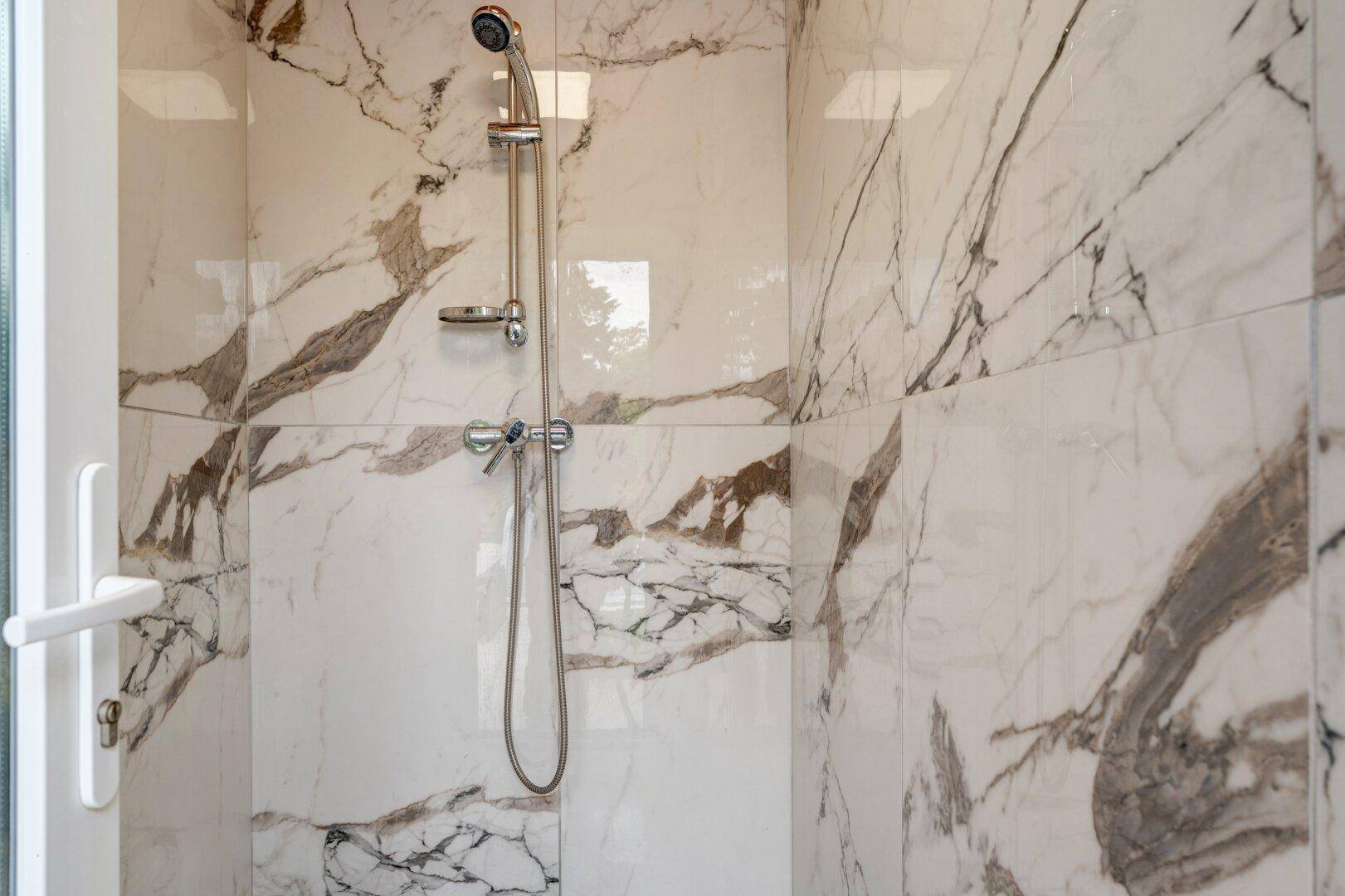 Moderne Duschkabine mit eleganten Marmorfliesen und verchromter Armatur.