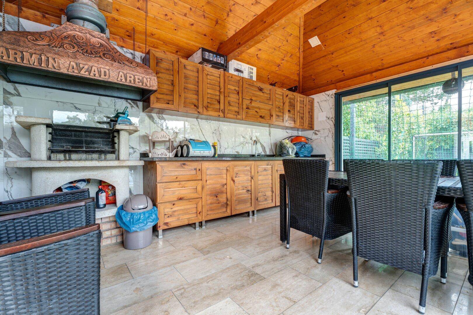 Rustikale Außenküche mit Holzschränken, integriertem Grill und Essbereich unter Holzdach.