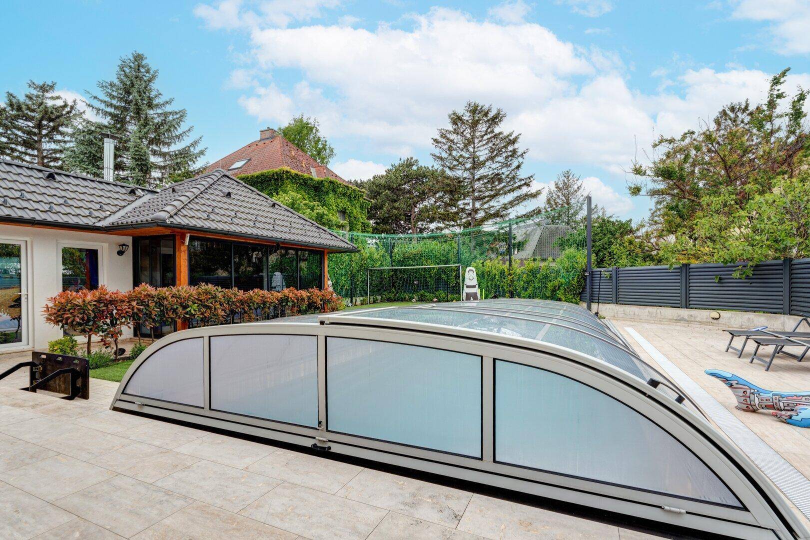 Überdachter Poolbereich mit gepflasterter Terrasse und Blick auf das Wohnhaus.