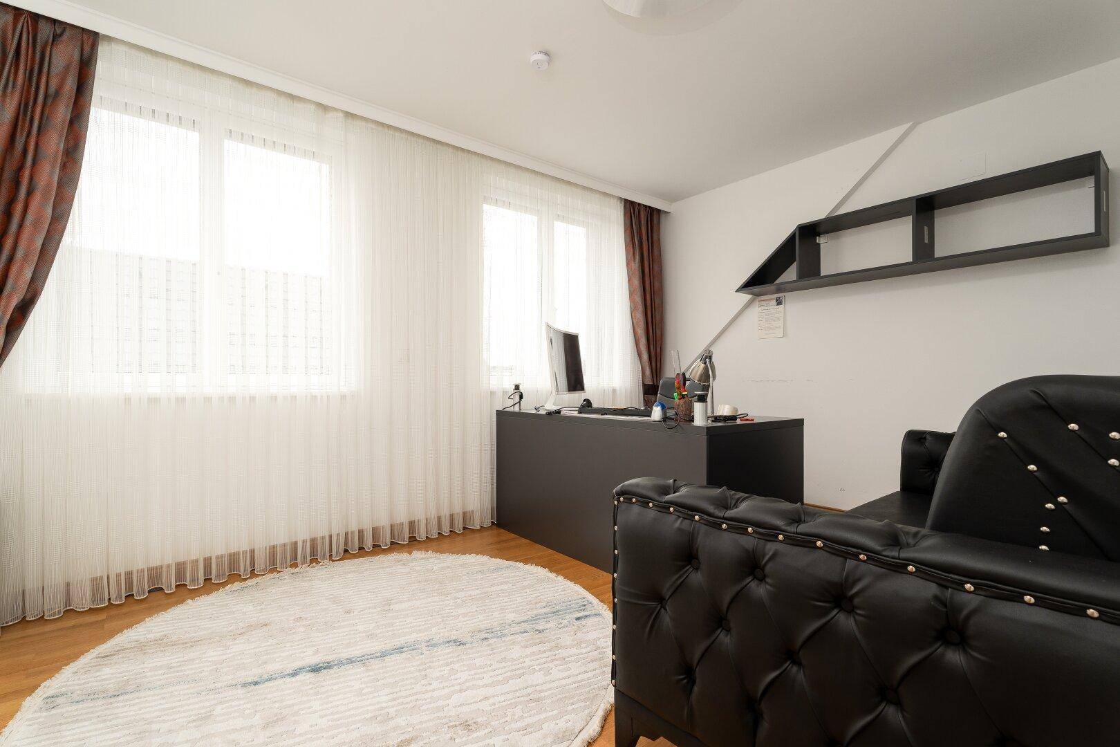Helles Arbeitszimmer mit großem Schreibtisch, bequemer Couch und großen Fenstern.