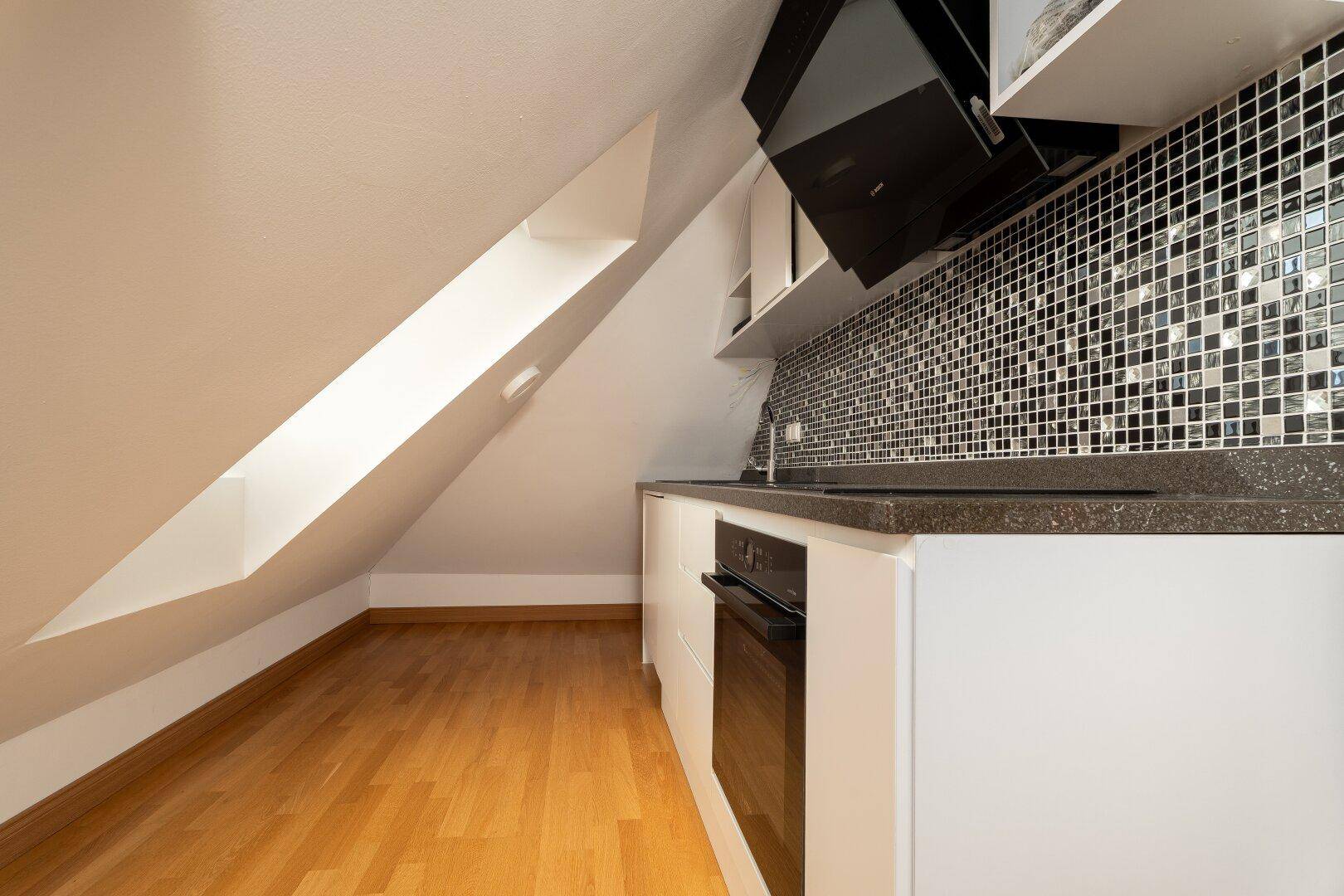 Kompakte Küche im Dachgeschoss mit modernen weißen Schränken und Mosaikfliesen.