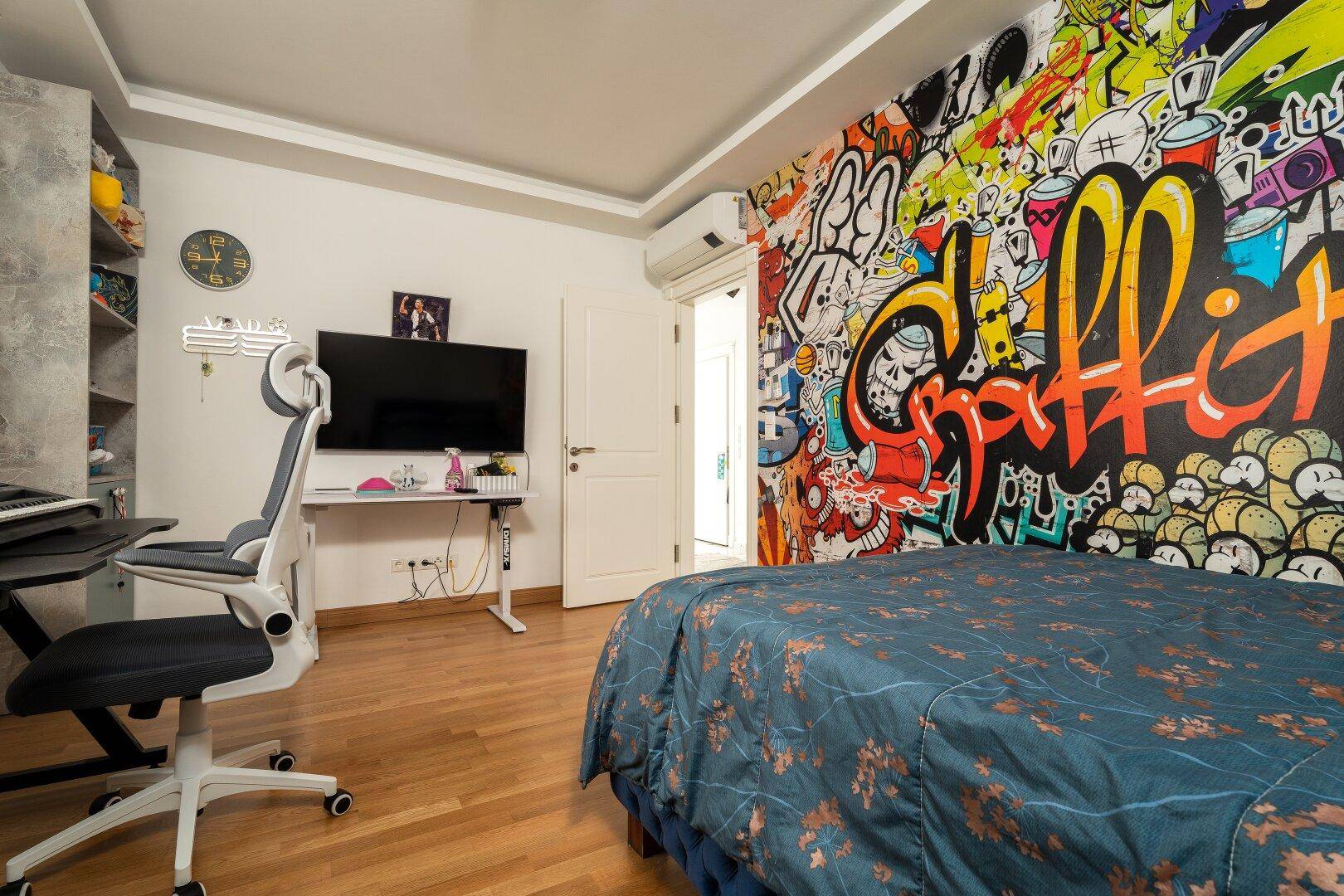 Schlafzimmer mit lebhafter Graffiti-Wand, Fernseher und Schreibtisch für kreative Nutzung.