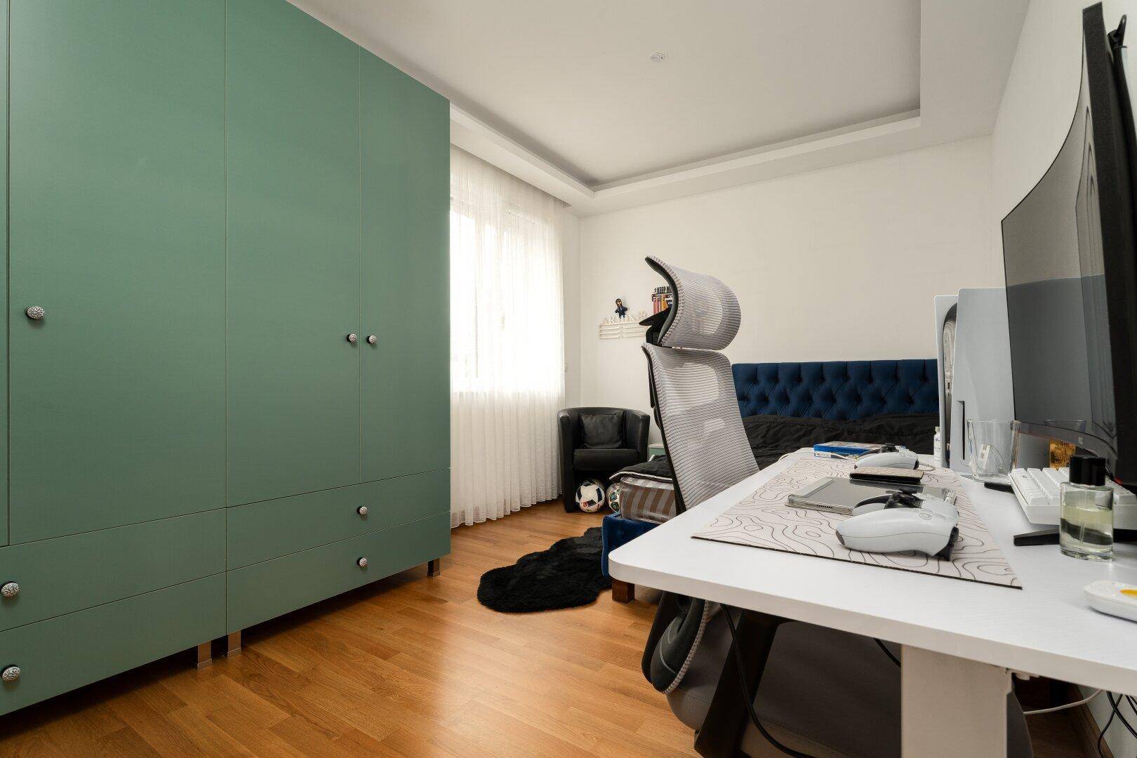 Helles Schlafzimmer mit großem grünem Kleiderschrank und modernem Arbeitsplatz.