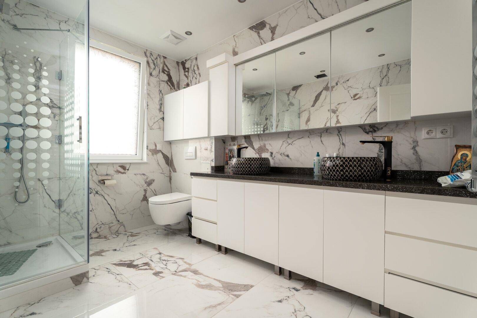 Luxuriöses Badezimmer mit Doppelwaschbecken, großer Dusche und eleganten Marmorfliesen.