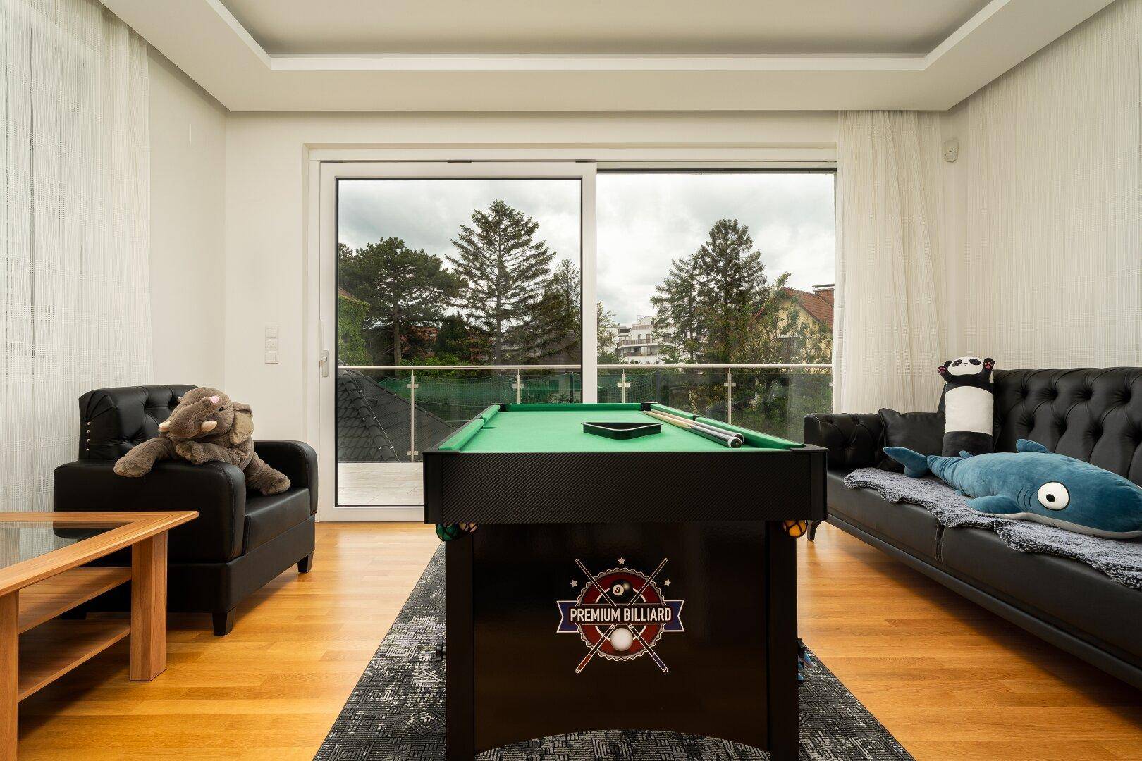 Geräumiges Wohnzimmer mit Billardtisch, bequemen Sofas und Zugang zu einem Balkon mit Blick ins Grüne.