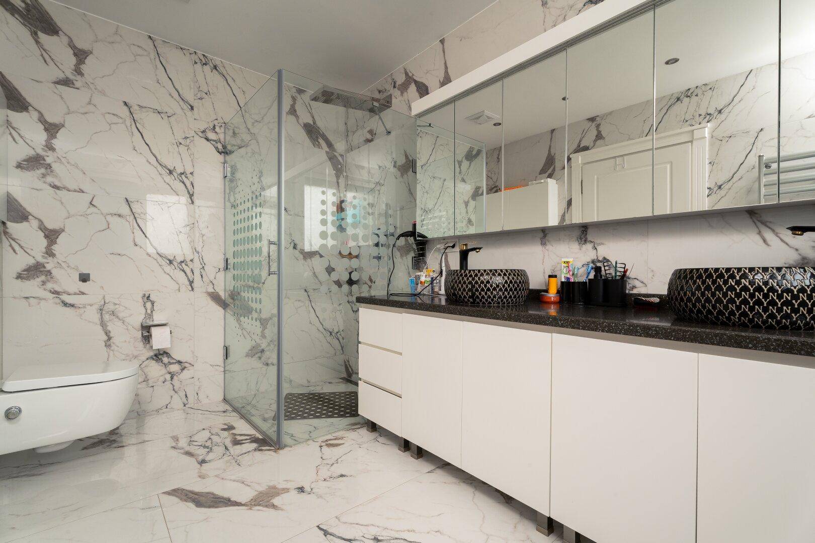 Luxuriöses Badezimmer mit Marmorfliesen, einer begehbaren Dusche und einem Doppelwaschbecken.
